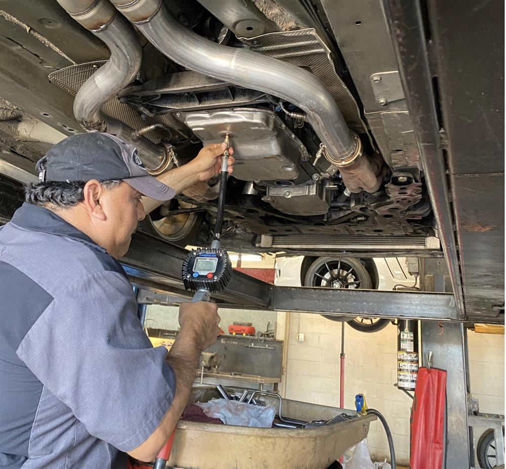 A person standing underneath a vehicle uses a computer sensor to diagnose transmission problems